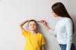 © Pixel-Shot - Mother measuring height of her son near wall