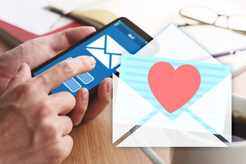 Wall Mural - Love messages concept. Closeup of male hands touching smartphone screen at table.Heart, mail icon and smartphone.