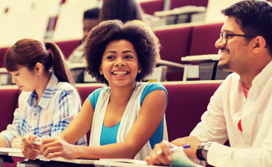 Poster - education, high school, university, learning and people concept - group of international students with notebooks writing in lecture hall