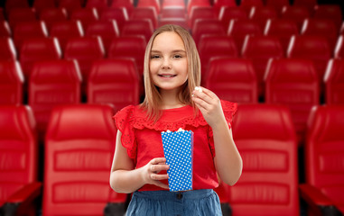 cinema, fast food and entertainment concept - beautiful smiling girl eating popcorn from blue paper bucket over movie theater background