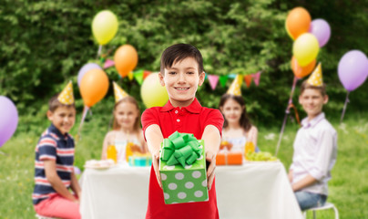 Wall Mural - childhood and people concept - smiling little boy in red polo t-shirt with gift box at birthday party over friends in summer park background