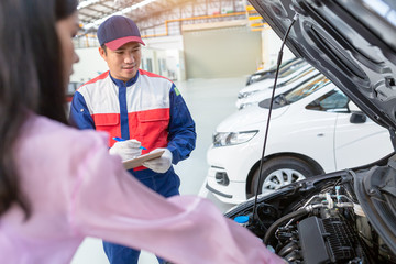 Wall Mural - Asian car mechanic and customer Woman talking to a car mechanic in Car service center, both are standing next to the car.