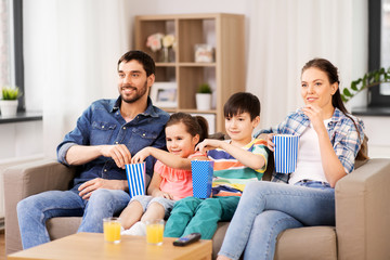 Wall Mural - family, leisure and people concept - happy mother, father, son and daughter with popcorn watching tv at home