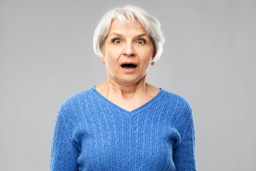 Wall Mural - emotion, expression and old people concept - portrait of shocked senior woman in blue sweater with open mouth by hands over grey background