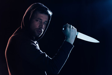 criminal in casual clothes holding knife and looking at camera on black