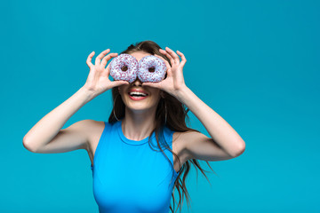 Wall Mural - smiling girl in swimsuit holding donuts isolated on blue