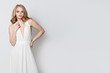 © millaf - Beautiful woman wearing white evening gown posing against white wall background