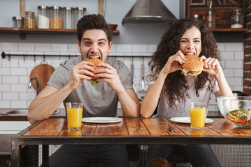 Poster - Cheerful couple eating burgers at the kitchen