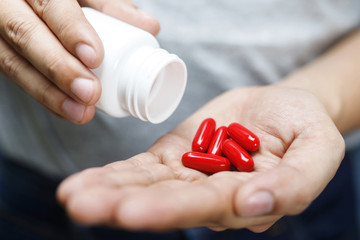 Wall Mural - close up man hand holding a medicine, with pours the pills vitamin out of the bottle. Caring for the health care