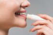 © LIGHTFIELD STUDIOS - cropped view of cheerful girl holding lip balm near lips isolated on grey