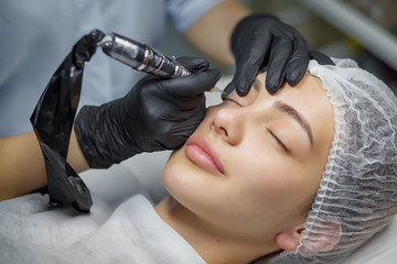 Wall Mural - Permanent make up eyeliner procedure, applying on young girl. Close-up. Young beautiful woman making permanent makeup in cosmetology salon. Young girl applying permanent eyeliner in beauty studio