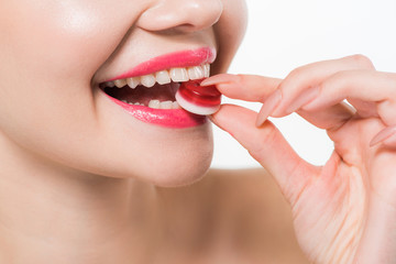 cropped view of cheerful girl eating red jelly candy isolated on white