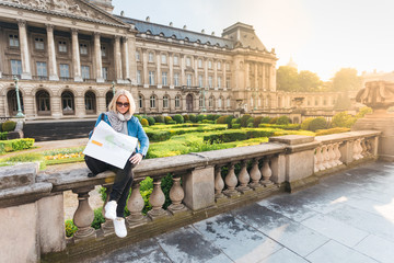 Wall Mural - Young girl tourist sits on the background of the Royal Palace in Brussels and looks into the city map, Belgium