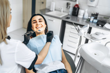 Pretty young female dentist making examination and treatment for young female patient in dental clinic.