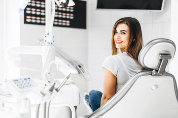 Wall Mural - Pretty happy and smiling dental patient sitting in the dental chair at the dental office.