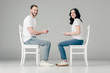 © LIGHTFIELD STUDIOS - smiling man and woman in white t-shirts and blue jeans sitting on chairs and using smartphones on grey background
