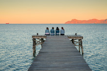 Women Sitting On The Pier And Talk Together. Mallorca, Spain. Summer Vacation With Friends