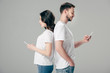 © LIGHTFIELD STUDIOS - focused man and woman in white t-shirts standing back to back and using smartphones isolated on grey