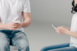 © LIGHTFIELD STUDIOS - cropped view of young man and woman using smartphones on grey background