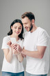© LIGHTFIELD STUDIOS - cheerful man and woman in white t-shirts with usb cable around hands using smartphone isolated on grey