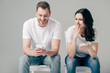 © LIGHTFIELD STUDIOS - shocked girl looking at boyfriend using smartphone isolated on grey