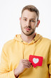 © LIGHTFIELD STUDIOS - thoughtful young man holding red paper cut card with heart symbol and looking at camera isolated on white