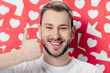 © LIGHTFIELD STUDIOS - handsome cheerful man showing thumb up near red paper cut cards with hearts symbol and looking at camera