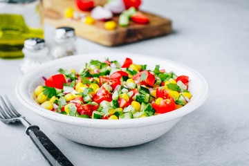 Fresh summer corn salad bowl with tomatoes, cucumbers, red onions and parsley.