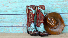 Pair Of Colorful Blue And Red Cowboy Boots And Hat Standing On A Natural Wood With A Blue Wooden Background