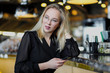 © spaskov - A young beautiful blond woman with glasses sits at the bar in a yellow interior. Drinks alcoholic cocktail with a straw and green mint.