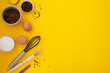 Ingredients for baking with baking utensile on yellow background - flour, wooden spoon, rolling pin, eggs, coccoa, sprinkles, banana. Top view, copy space.