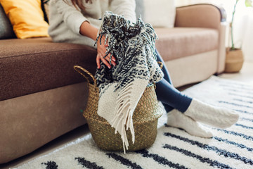 Young woman puts blanket in straw basket. Interior decor of living room