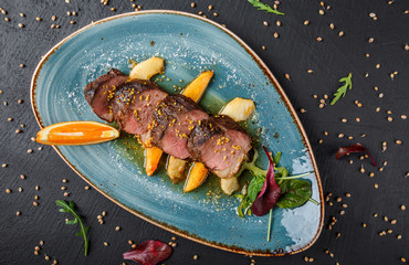 Wall Mural - Juicy duck breast steaks with caramelized fruit, mango, apple and sauce of orange on plate over dark stone background. Hot Meat Dishes. Top view.