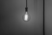 An Old Vintage Electric Light Bulb Hanging On The Air. Detaile Shot Of A Glass Ligh Bulb Shining. Old Metal And Glass Bulb. Black And White Background Fine Art Photo.
