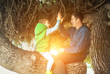 Happy childhood, father and son sit on a tree on a sunny day, fa