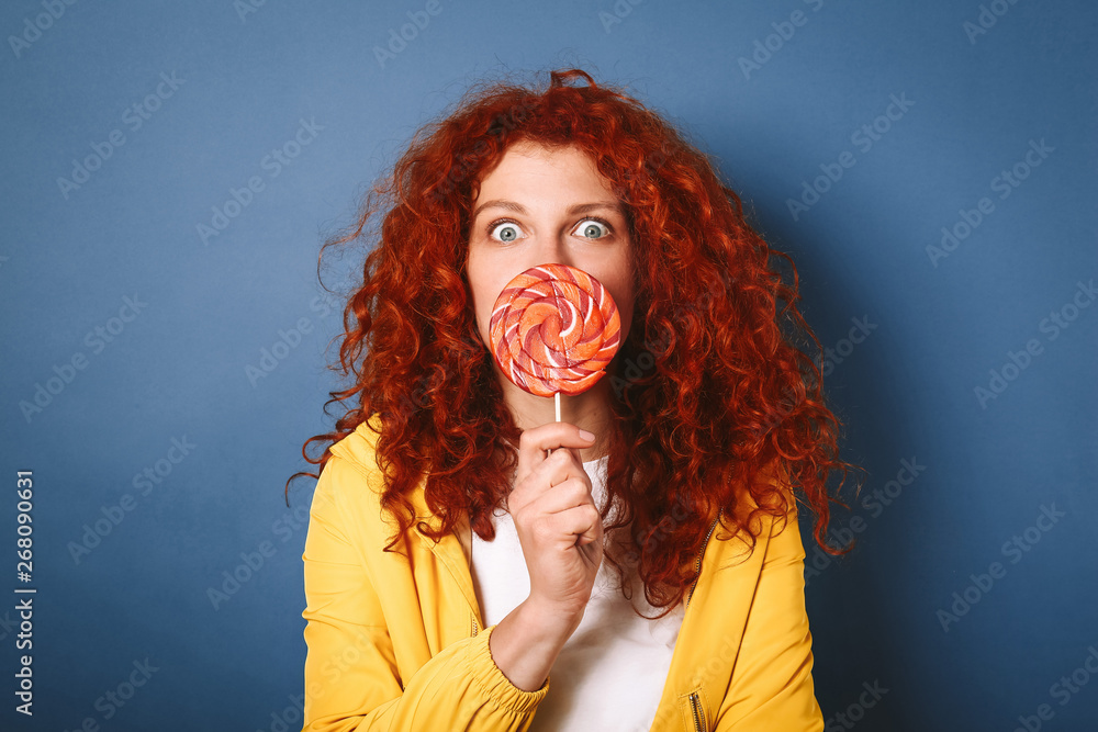 Funny redhead woman with lollipop on color background