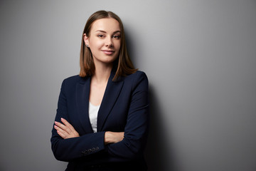 Confidence and charisma. Young business woman in suit looking at camera. Grey background.