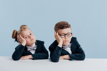 Wall Mural - education. two schoolchildren are exhausted, sitting at the white table, isolated on blue background, copy space, school concept