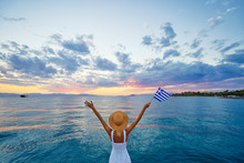 Enjoying Vacation In Greece. Young Traveling Woman With National Greek Flag Enjoying Sunset On Sea.