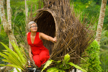 Wall Mural - attractive and happy middle aged 40s or 50s Asian tourist woman with grey hair and elegant red dress sitting outdoors at tropical jungle relaxed admiring beauty of nature