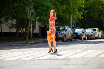 Poster - Young beautiful blonde woman in a red flower dress crosses the road at a crosswalk