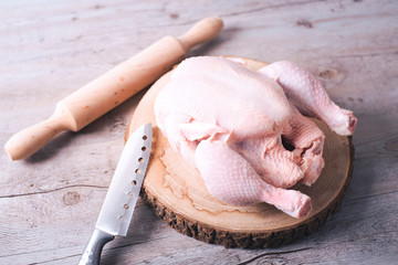 Raw chicken on wooden table next to knife and rolling pin. Food