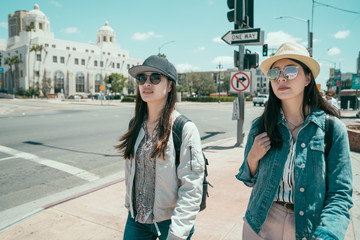 two young asian women tourist walking together on city street. female college friends classmates out on road on summer day going to school university. beautiful sisters traveler in hat and sunglasses