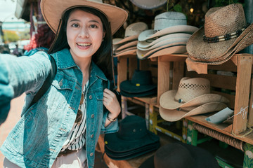 Wall Mural - Beautiful asian woman taking selfie buying hats at olvera street vendor. Consumerism shopping traveling lifestyle concept. young girl tourist make self photo wearing straw hat in local mexico market