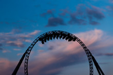 Silhouette Of People Having Fun On A Roller-coaster In An Amusement Park At Sunset. Adrenalin Concept.