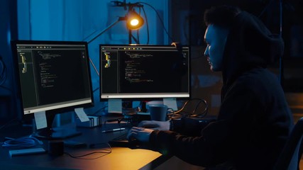 cybercrime, hacking and technology concept - asian male hacker using computer virus program for cyber attack and taking notes in dark room at night
