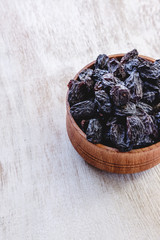 Wall Mural - Dark blue raisins in a wooden bowl on a bright white background. Close-up. Insulated.