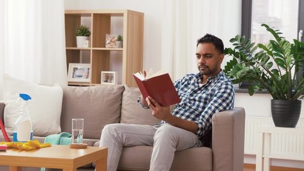 Sticker - household and people concept - indian man reading book and resting after home cleaning and drinking water from glass