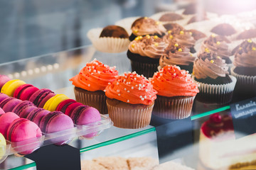 Showcase with sweets in the cafe. Cupcakes and colored macaroons on the cake display. Sweet desserts