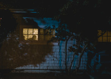 View Of A Silhouette In A Lighted Window From The Outside Of A House